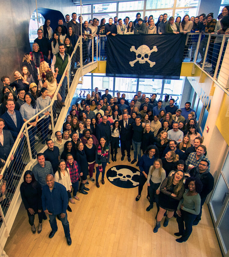 An entire agency of employees gathers in their TBWA office with the pirate flag flying.