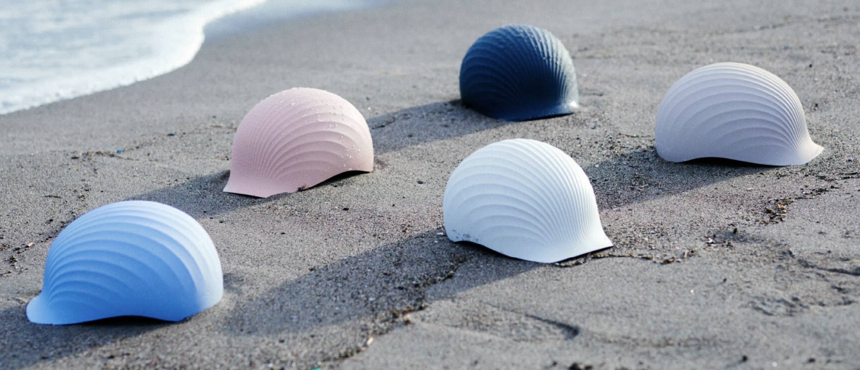 Five hardhats that resemble shells placed on the sand of a beach