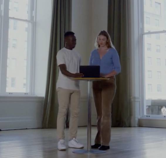 A man and woman standing around a table looking at a laptop