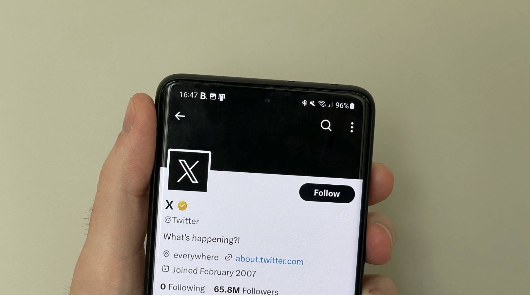 Hand holding a smartphone with Twitter's account X on the screen