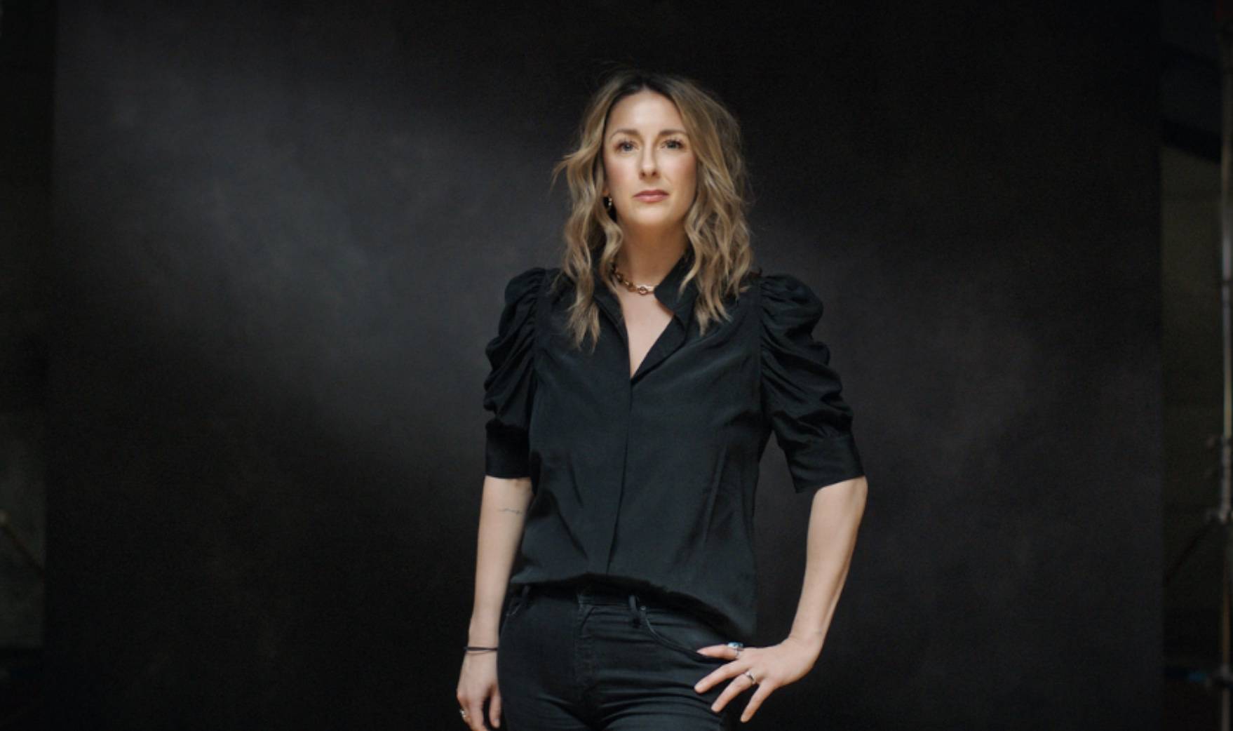 Headshot of Jen Costello wearing all black against a black backdrop