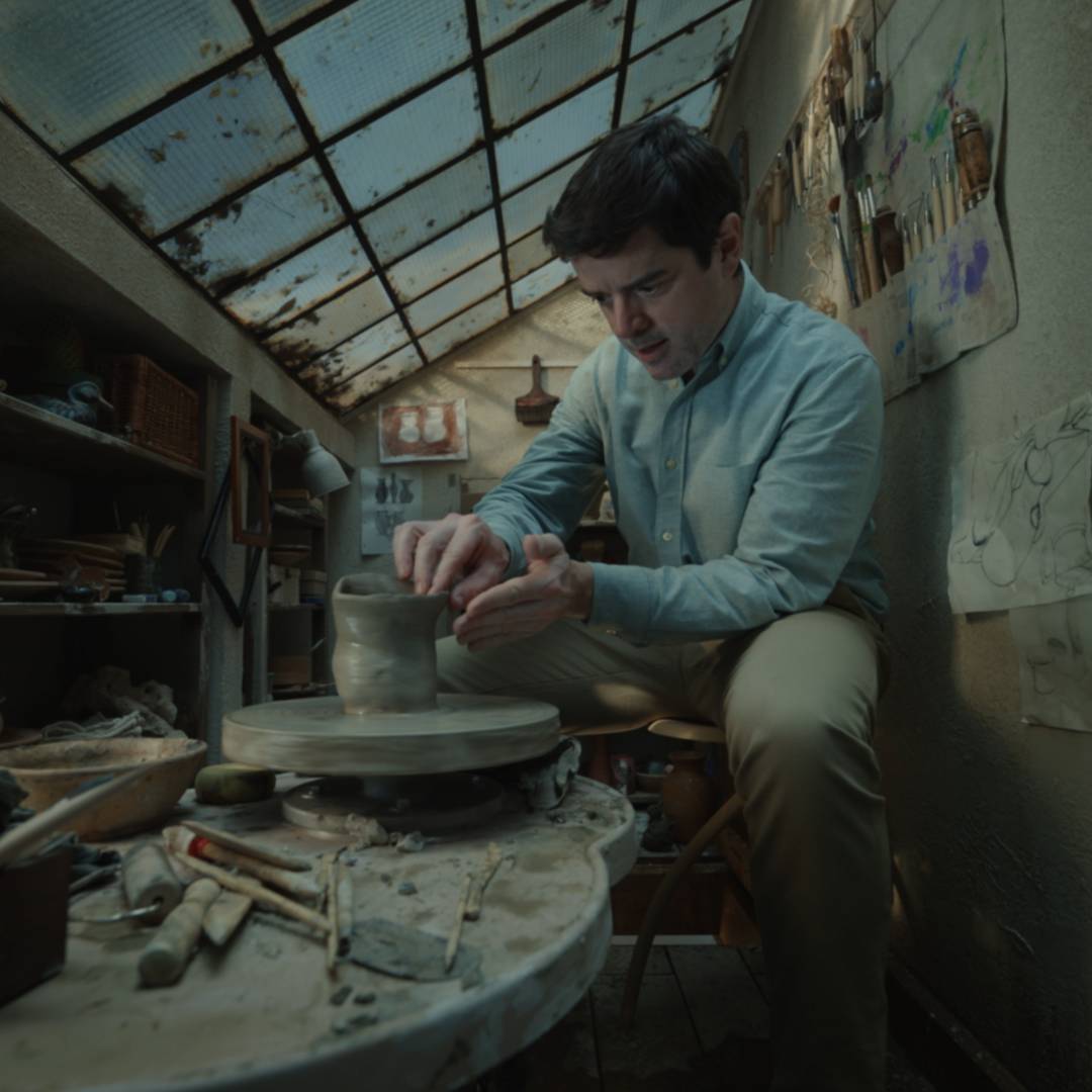 A man happily sits in a pottery studio built in a tiny, one square meter room.