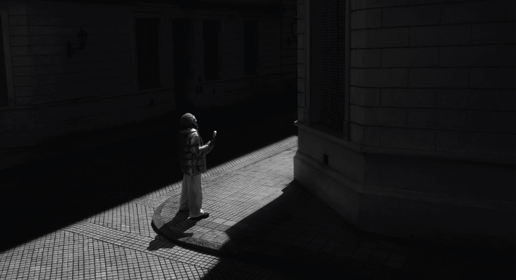 A woman in winter clothing stands in a ray of sun, eating a Magnum ice cream.
