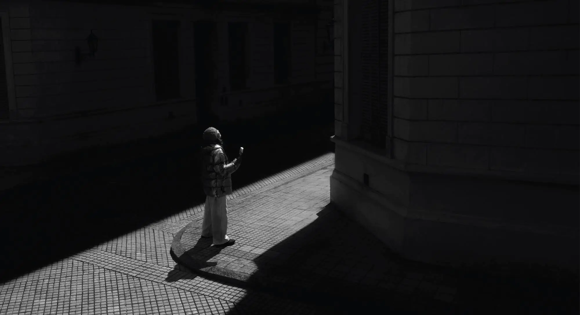 A woman in winter clothing stands in a ray of sun, eating a Magnum ice cream.